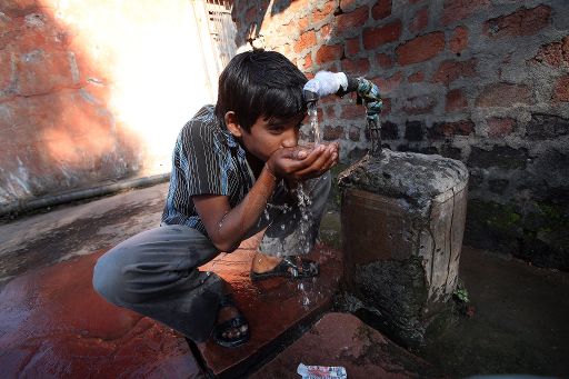 Ein indischer Junge trinkt Wasser aus einem Brunnen