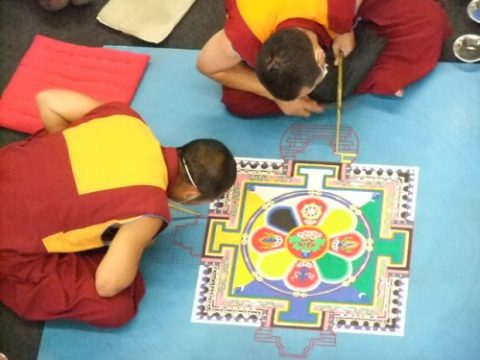 Buddhistische Mönche gestalten Mandala aus Sand im Triangel