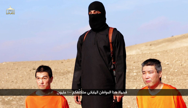 Die zwei japanischen Geiseln knien neben einem vermummten Mann