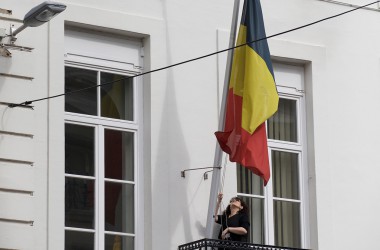 Frau hisst belgische Flagge an einem Gebäude in der Brüsseler Rue de la Loi