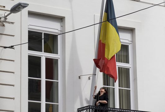 Frau hisst belgische Flagge an einem Gebäude in der Brüsseler Rue de la Loi
