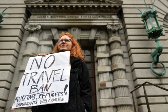 Frau vor Gerichtgebäude, hält Protestblatt hoch, Text: Nein zum Einreisestopp