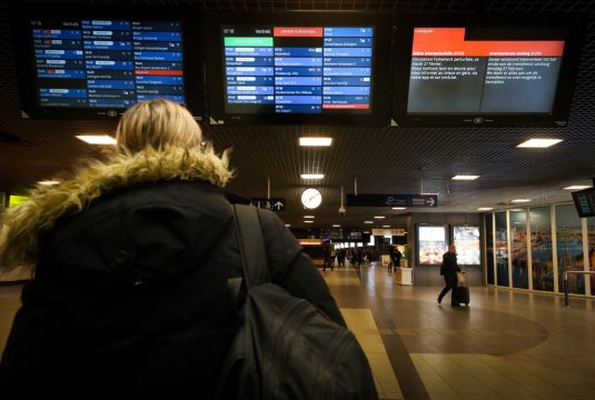 Eine Person steht in einer Bahnhofshalle und schaut auf die Informationstafeln, auf denen viele Zugausfälle vermerkt sind