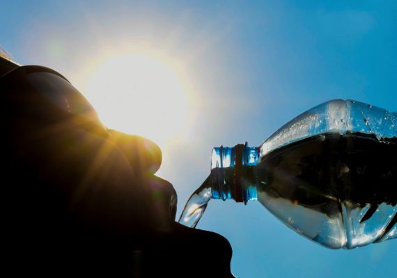 Mann trinkt aus Wasserflasche, im Hintergrund knallt die Sonne vom blauen Himmel