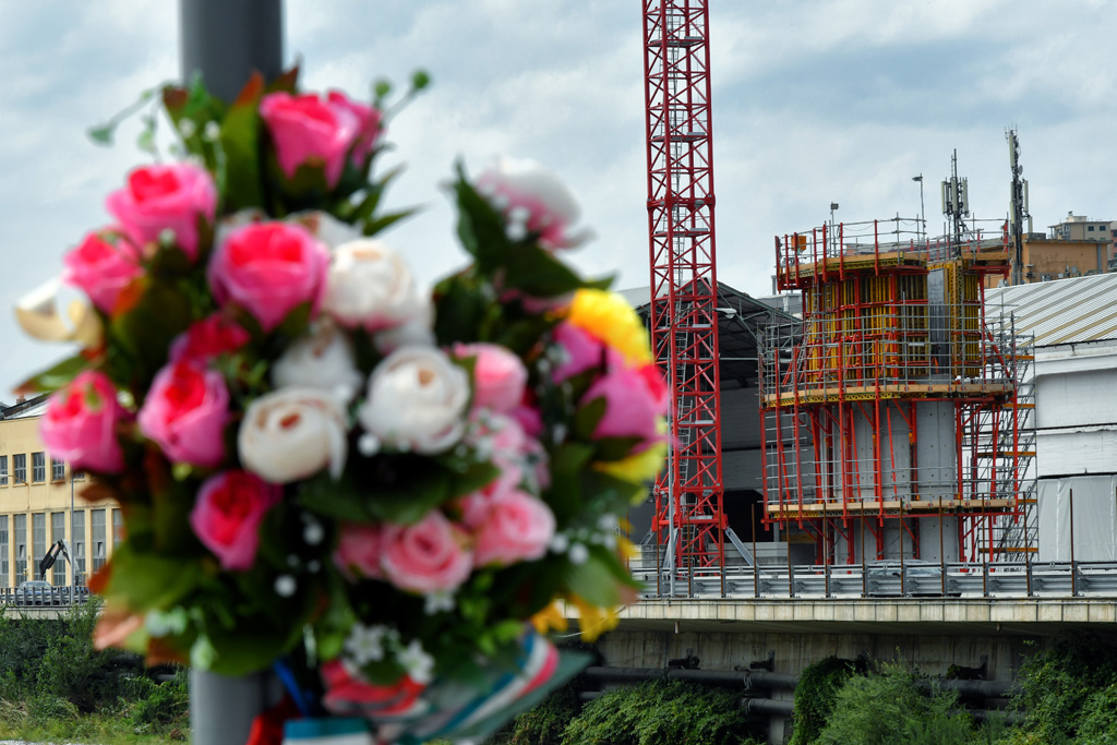 Blumen in Gedenken an die Opfer des Brückeneinsturzes - im Hintergrund: der erste Pfeiler der neuen Brücke in Genua (Bild: Alberto Pizzoli/AFP)