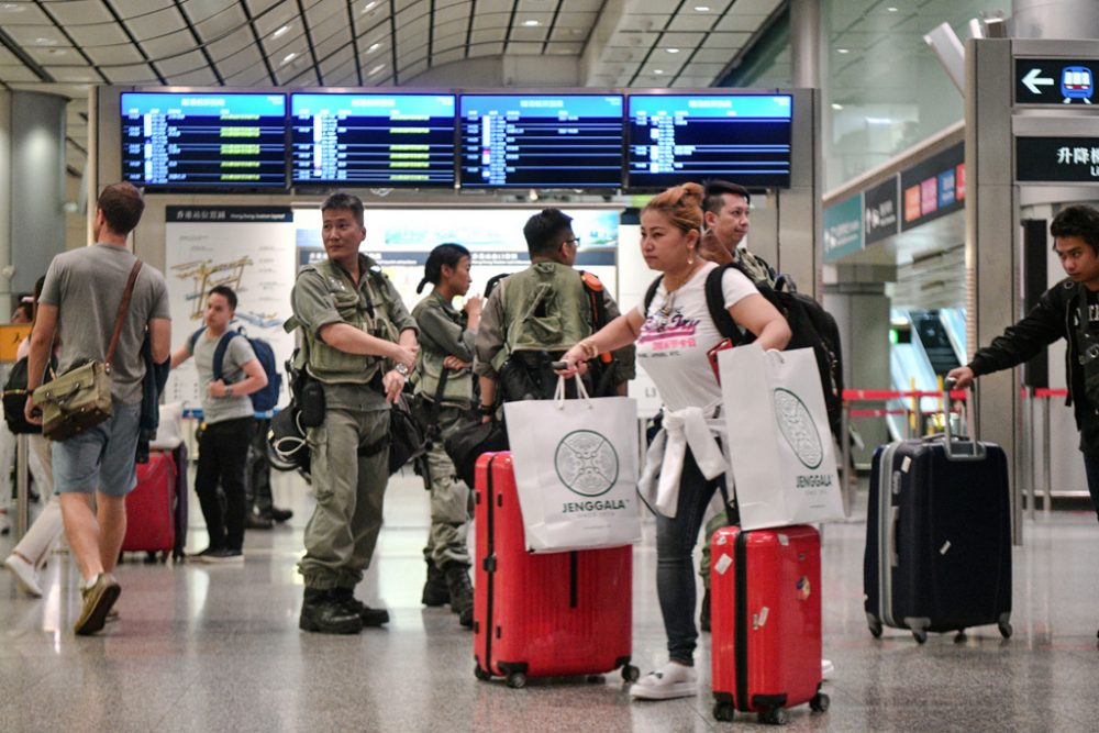 Passagiere am Hongkonger Flughafen rollen ihr Gepäck an Polizisten vorbei (Bild: Anthony WallaceAFP)