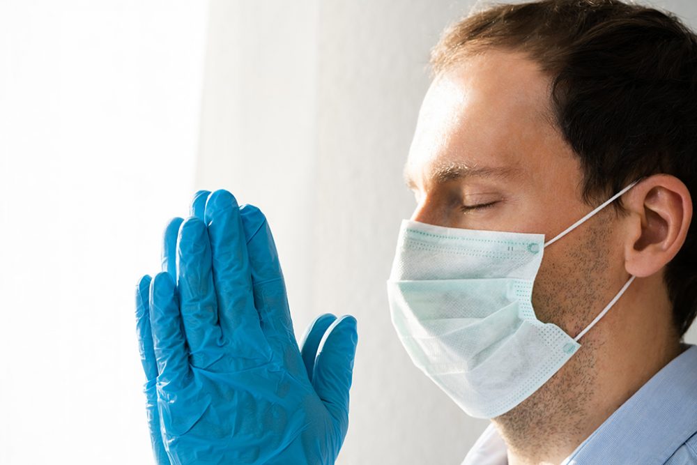 Mann mit Schutzmaske und Handschuhen betet während der Corona-Pandemie (© Bildagentur PantherMedia / Andriy Popov)