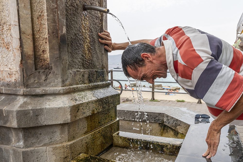 Ein Mann sucht angesichts der hohen Temperaturen Abkühlung an einer Trinkwasserstelle in Messina auf Sizilien (Bild: Giovanni Isolino/AFP)