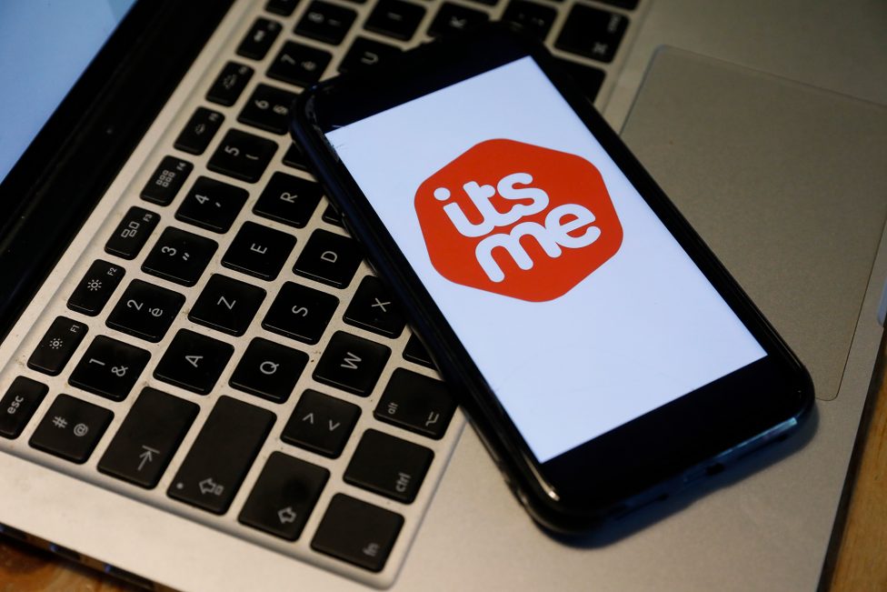 Das Logo der Itsme-App auf dem Display eines Smartphones, das auf einer Laptoptastatur liegt
