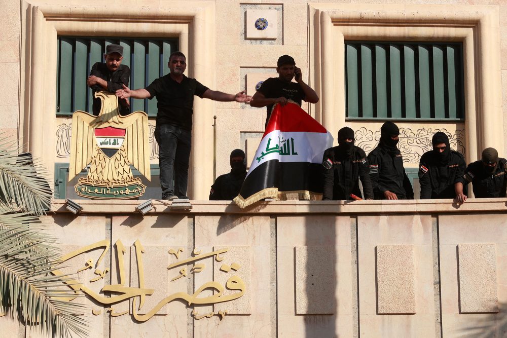 Sicherheitskräfte stehen Wache, als sich Anhänger des irakischen schiitischen Geistlichen Muktada al-Sadr auf dem Balkon des Regierungssitzes in der Grünen Zone der Hauptstadt Bagdad versammeln (Bild: Ahmad Al-Rubaye/AFP)