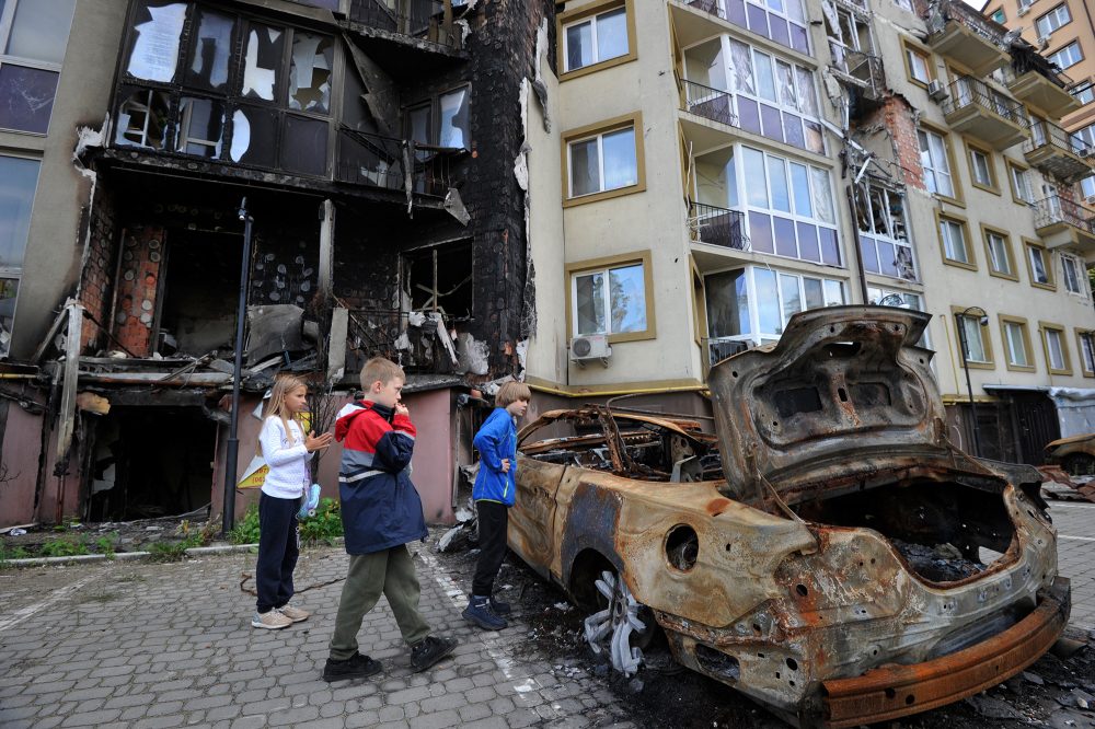 Kinder vor zerstörtem Haus und Auto