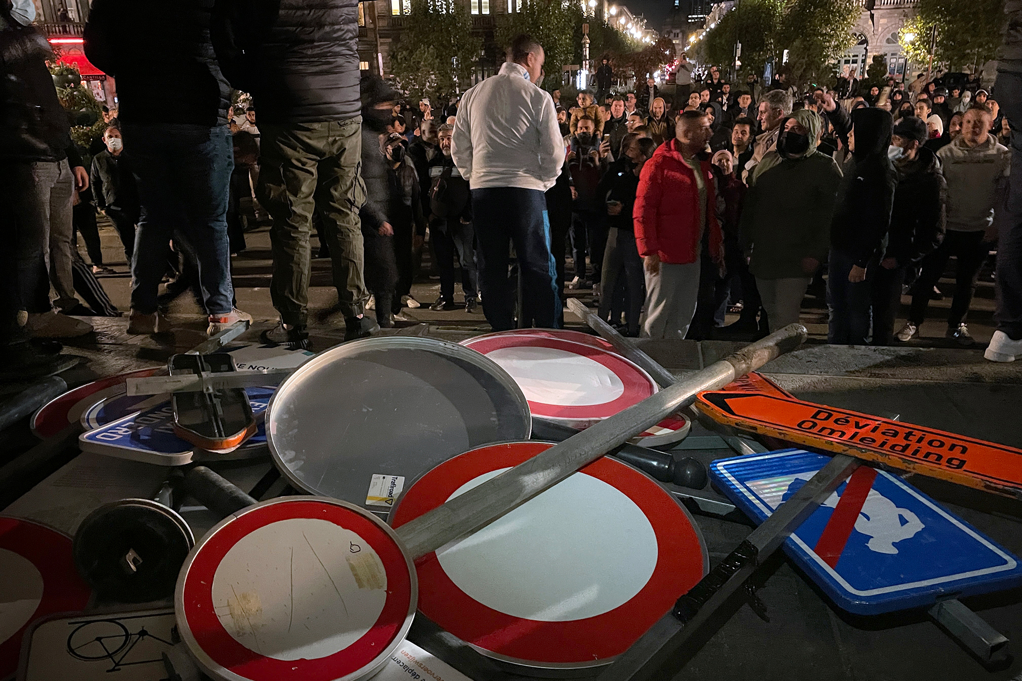 Zerstörte Verkehrsschilder neben protestierenden Menschen in Schaerbeek (Bild: Nils Quintelier/Belga)