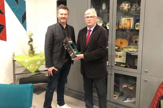 Zum Abschied vom Schöffenamt erhält Charles Servaty (re.) von Bütgenbachs Bürgermeister Daniel Franzen einen edlen Tropfen (Bild: Dogan Malicki/BRF)