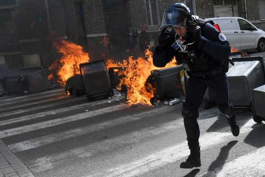 Ein französischer Polizist rennt während einer Demonstration in Rennes an brennenden Mülleimern vorbei (Bild: Jean-François Monier/AFP)