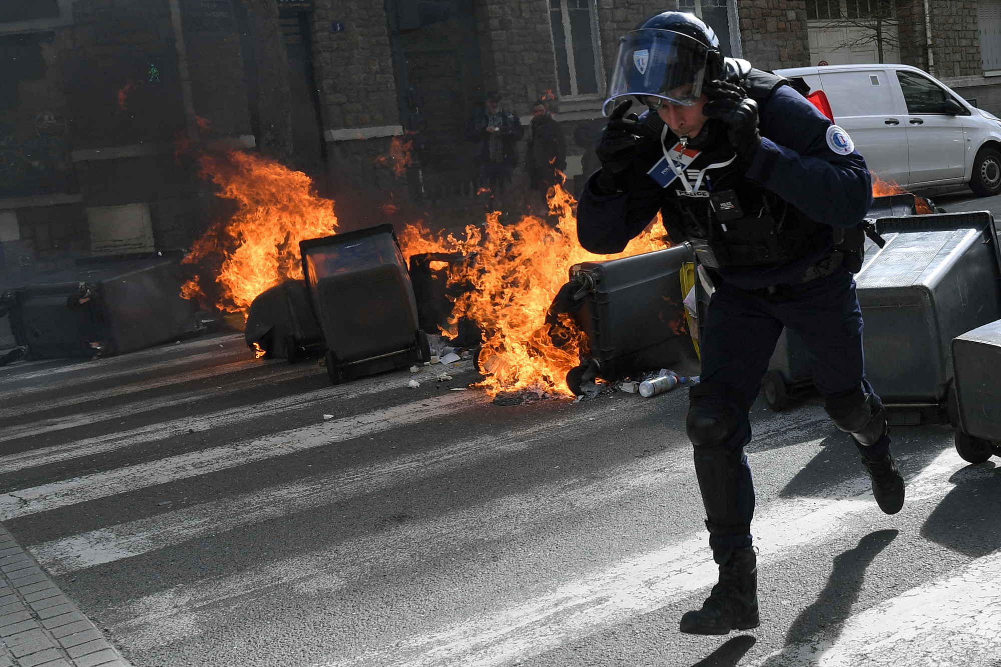 Ein französischer Polizist rennt während einer Demonstration in Rennes an brennenden Mülleimern vorbei (Bild: Jean-François Monier/AFP)