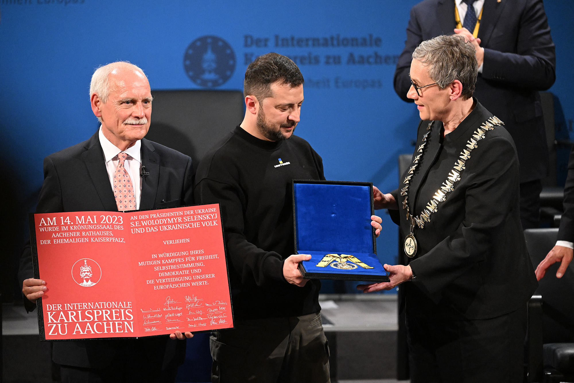 Wolodymyr Selenskyj nimmt den Karlspreis entgegen von Aachens Bürgermeisterin Sibylle Keupen und dem Vorsitzenden des Karlspreis-Direktoriums, Jürgen Linden (Bild: Ina Fassbender/AFP)