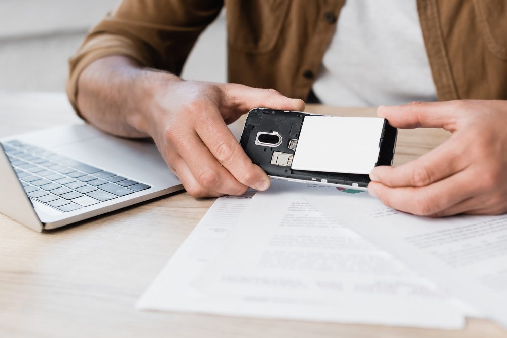 Geschäftsmann, der am Arbeitsplatz Akku in Handy steckt