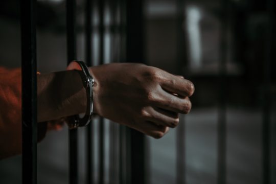 Hand mit Handschallen an einem Gefängnisgitter