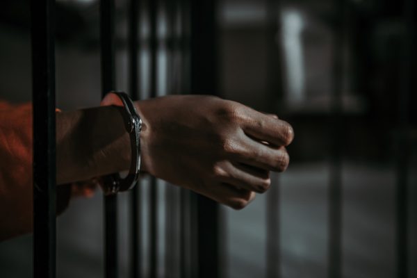 Hand mit Handschallen an einem Gefängnisgitter