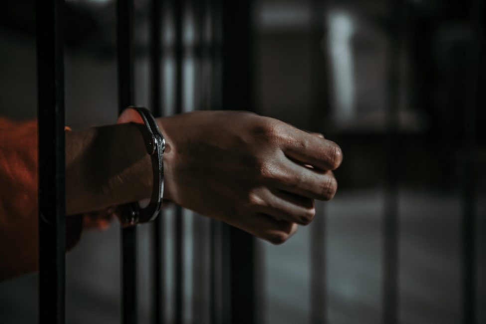 Hand mit Handschallen an einem Gefängnisgitter