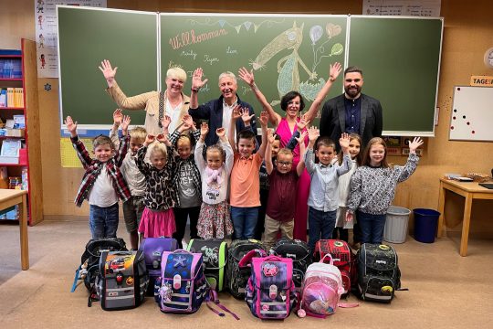 (vlnr.) Die I-Dötzchen der Honsfelder Schule zusammen mit Schöffin Viviane Scharres, Bürgermeister Friedhelm Wirtz, Lehrerin Béatrice Gassmann und Patrick Vahlefeld, der am Freitag ebenfalls seinen ersten Schultag hat als neuer Direktor der Gemeindeschulen Büllingen, Mürringen und Honsfeld (Bild: Julia Slot/BRF)