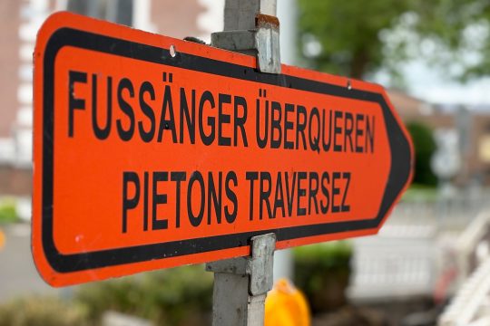 Hinweisschild: Straßenarbeiten - Fußgänger bitte überqueren