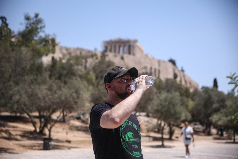 Ein Tourist trinkt Wasser, während er bei heißen Temperaturen in der Nähe der Akropolis in Athen steht