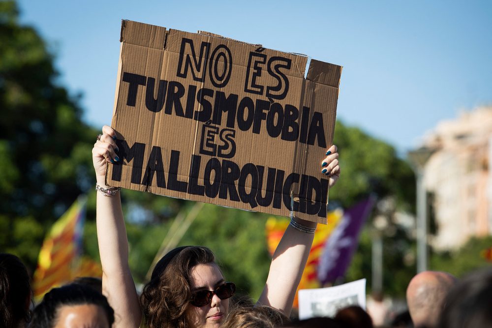 Eine Frau hält ein Protest-Plakat in die Höhe während einer Demonstration gegen Übertourismus und die Immobilienpreise auf der Insel Mallorca