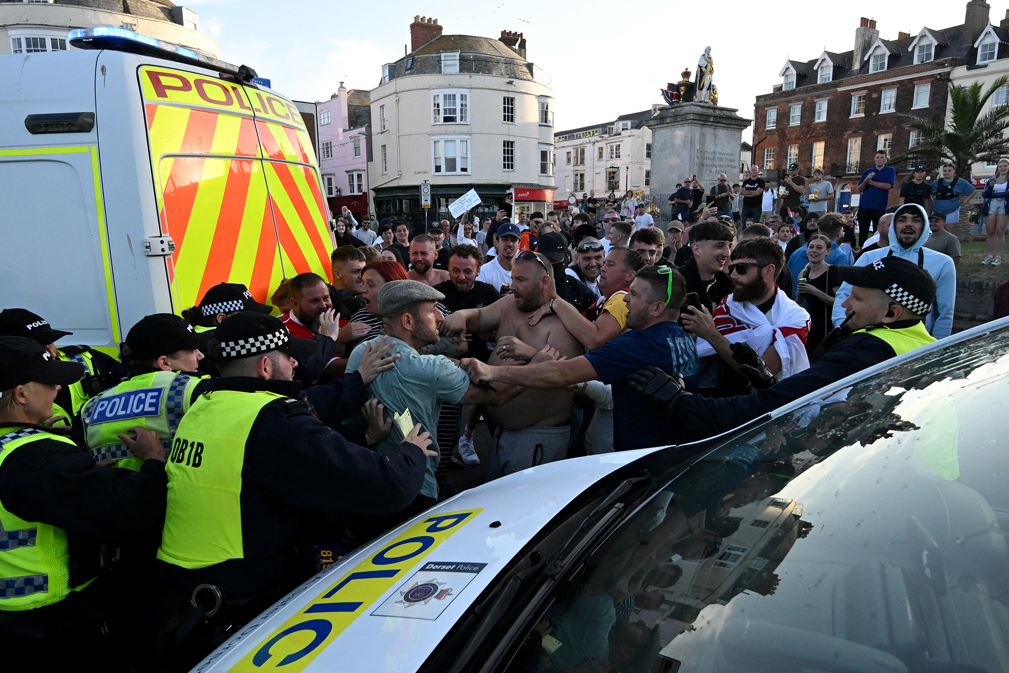 Polizeibeamte stehen Demonstranten gegenüber, zu der rechtsextreme Aktivisten am 4. August 2024 in Weymouth an der Südwestküste Englands aufgerufen haben, wo das Migrantenschiff Bibby Stockholm vor Anker liegt