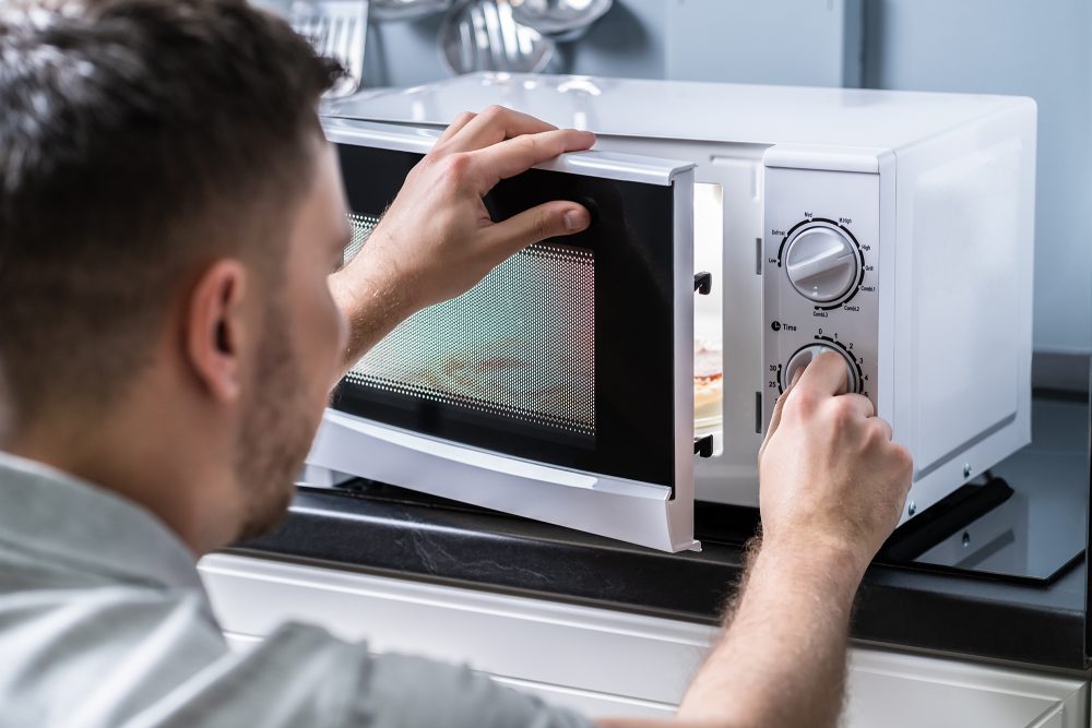 Junger Mann bereitet Essen in Mikrowelle auf Küchentheke zu