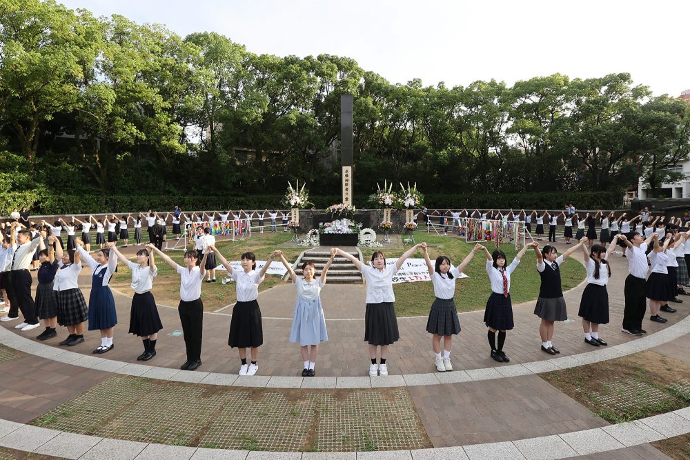 Oberschüler umringen in Nagasaki anlässlich des 79. Jahrestags des Atombombenabwurfs auf die Stadt das Denkmal, das das Zentrum der Atombombenabwürfe markiert, mit einer Menschenkette, um eine friedliche Welt zu fordern