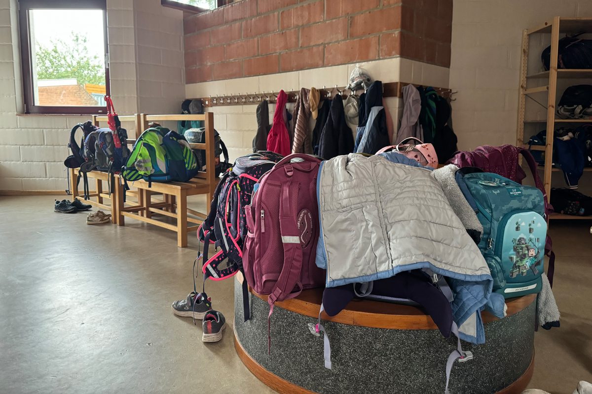 Auf dem Bild sind Jacken, Rucksäcke und Schuhe zu sehen, die die in der außerschulischen Betreuung betreuten Kinder in Raeren ausgezogen haben, im Hintergrund Bänke und eine Garderobe