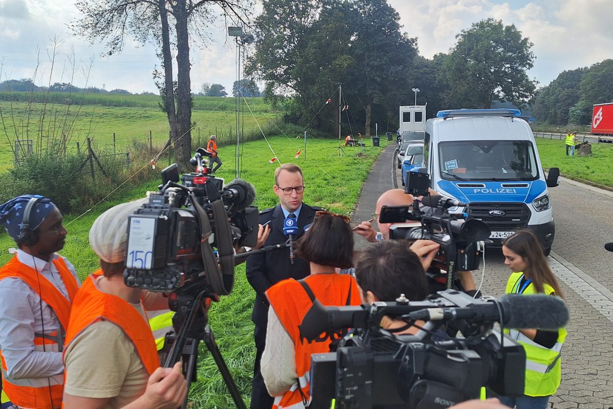 Mehrere Journalisten und Kameramänner mit ihrem Equipment scharen sich um den Sprecher der deutschen Bundespolizei, um ihn zu interviewen