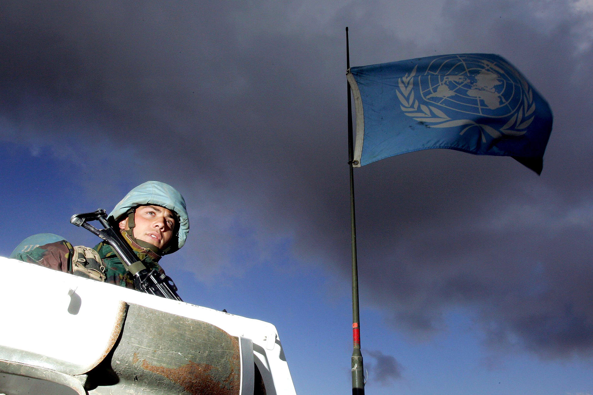 Ein Blauhelmsoldat steht auf einem Kampffahrzeug, im Hintergrund weht die Flagge der Vereinten Nationen