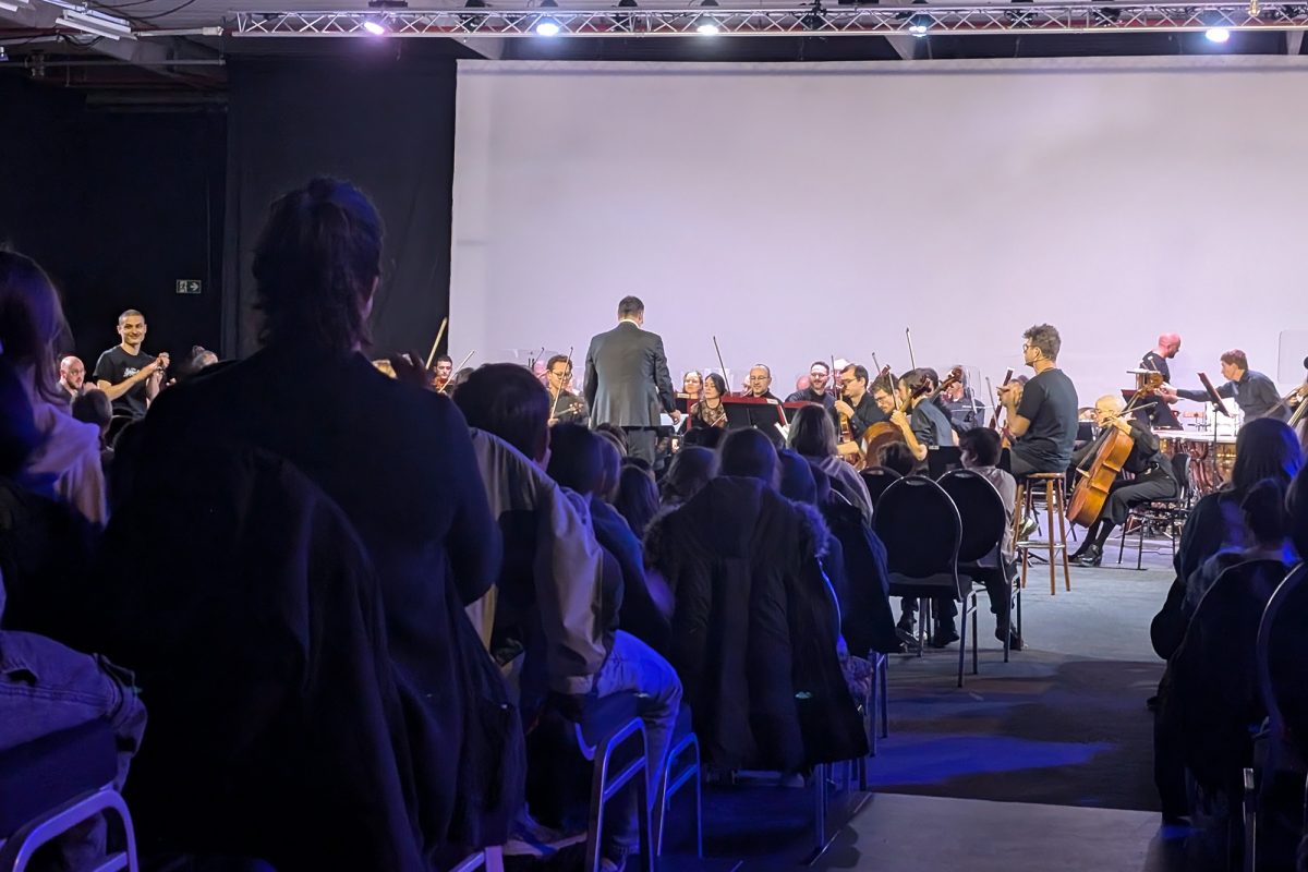 Das Orchester spielt auf der Bühne, davor sitzen viele Zuschauer im Saal