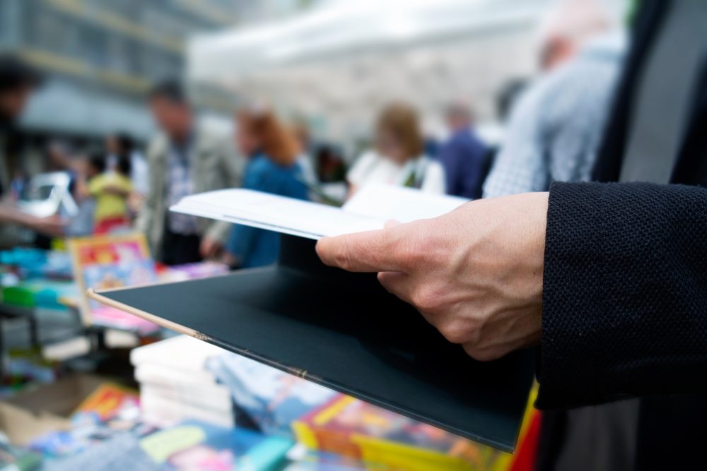 Besucher blättert durch ein Buch an einem Stand bei einer Buchmesse