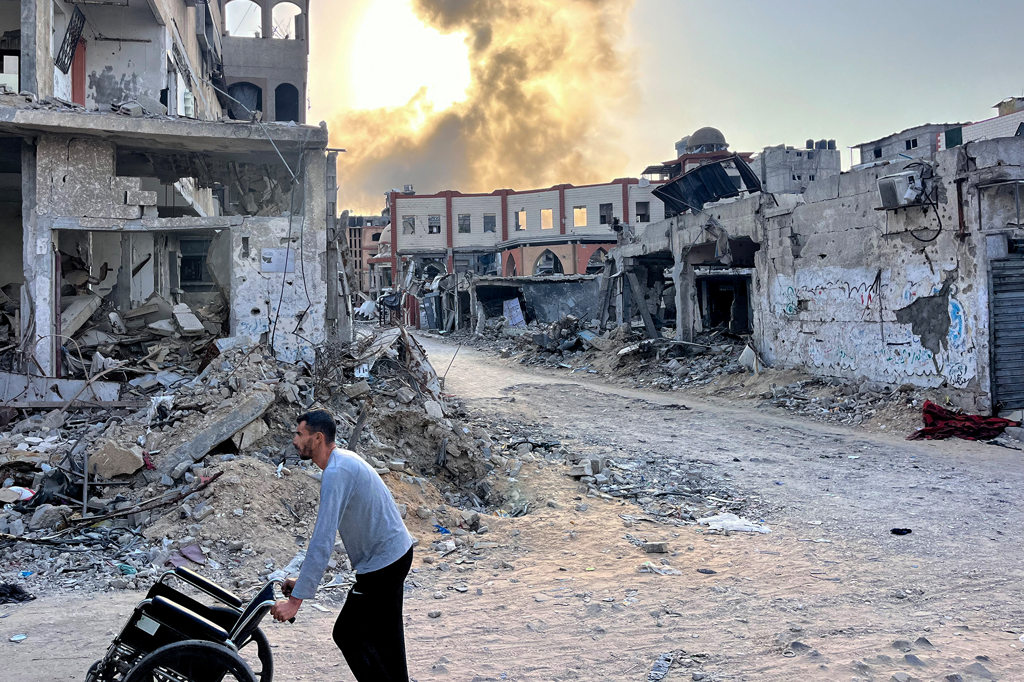 Rauch steigt nach einem israelischen Bombardement in Beit Lahia im nördlichen Gazastreifen auf, man sieht einen Mann, der einen leeren Rollstuhl schiebt