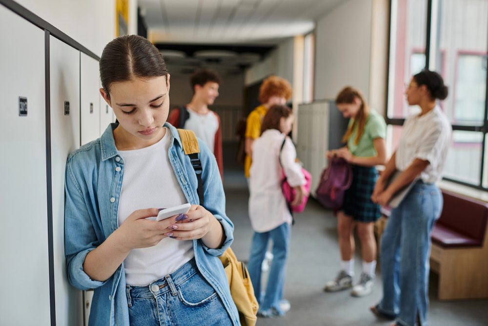 Mädchen textet auf Smartphone im Schulflur