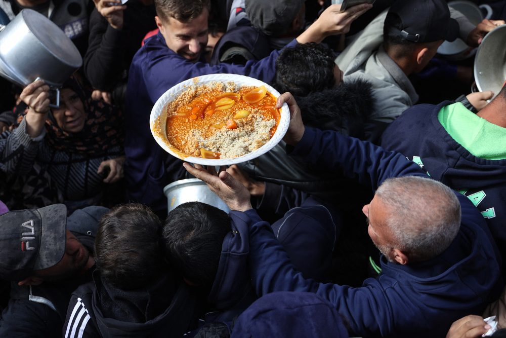 Ein Mann trägt einen Teller mit Essen, während Palästinenser humanitäre Hilfe abholen