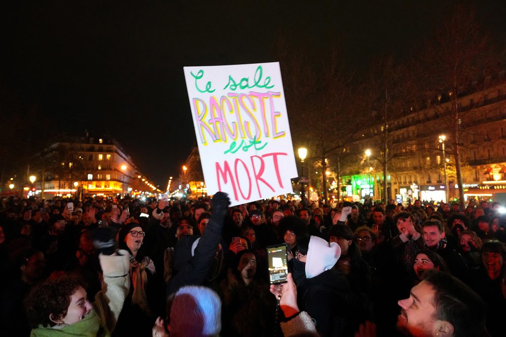 Ein Mann hält ein Plakat mit der Aufschrift „Der schmutzige Rassist ist tot“ hoch, während sich Menschen auf der Place de la Republique in Paris versammeln, um den Tod von Jean-Marie Le Pen zu feiern