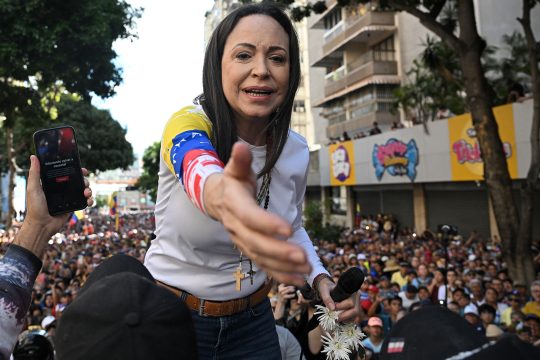 Die venezolanische Oppositionsführerin María Corina Machado streckt symbolisch die Hand aus bei einer Protestkundgebung in Caracas, im Hintergrund sind zahlreiche Demonstranten zu sehen