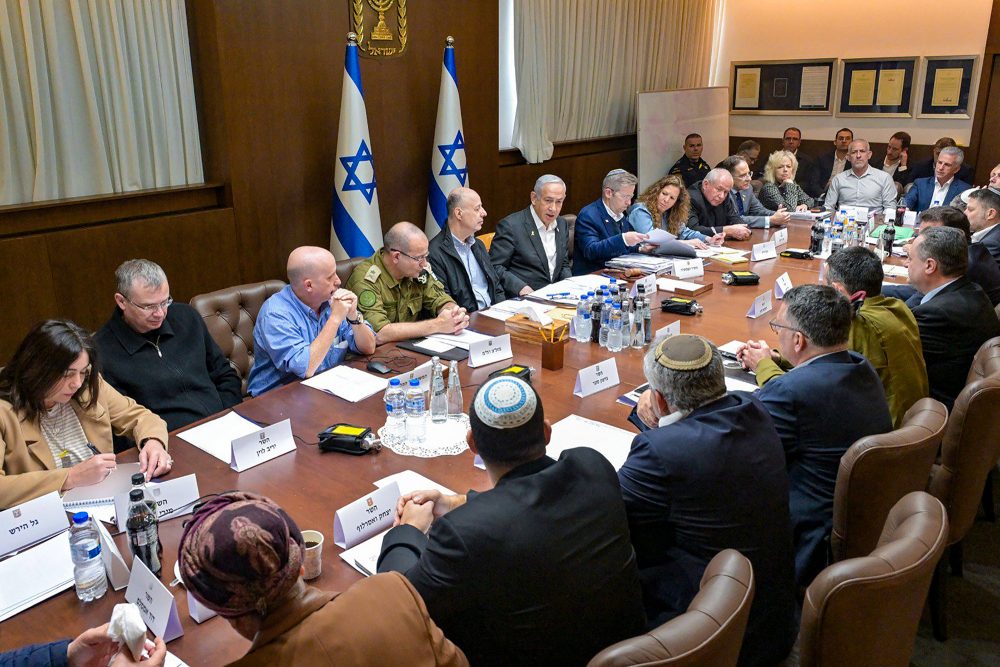 Mitglieder des israelischen Sicherheitskabinetts, unter ihnen Ministerpräsident Netanyahu, sitzen um einen langen Konferenztisch herum und beraten, im Hintergrund stehen zwei Nationalflaggen