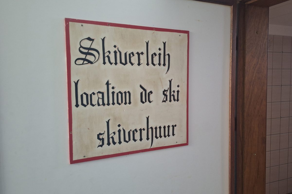 Ein Schild mit der dreisprachigen Aufschrift "Skiverleich - location de ski - skiverhuur"