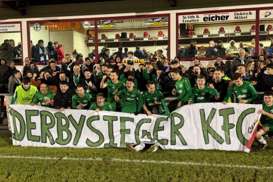 Jubelnde Spieler des FC Grün-Weiß Amel halten eine Banderole mit der Aufschrift "Derbysieger KFC"