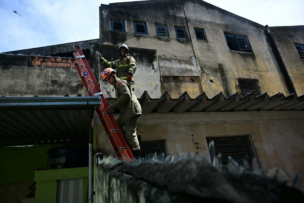 Feuerwehrleute auf einer Leiter vor der ausgebrannten Textilfabrik