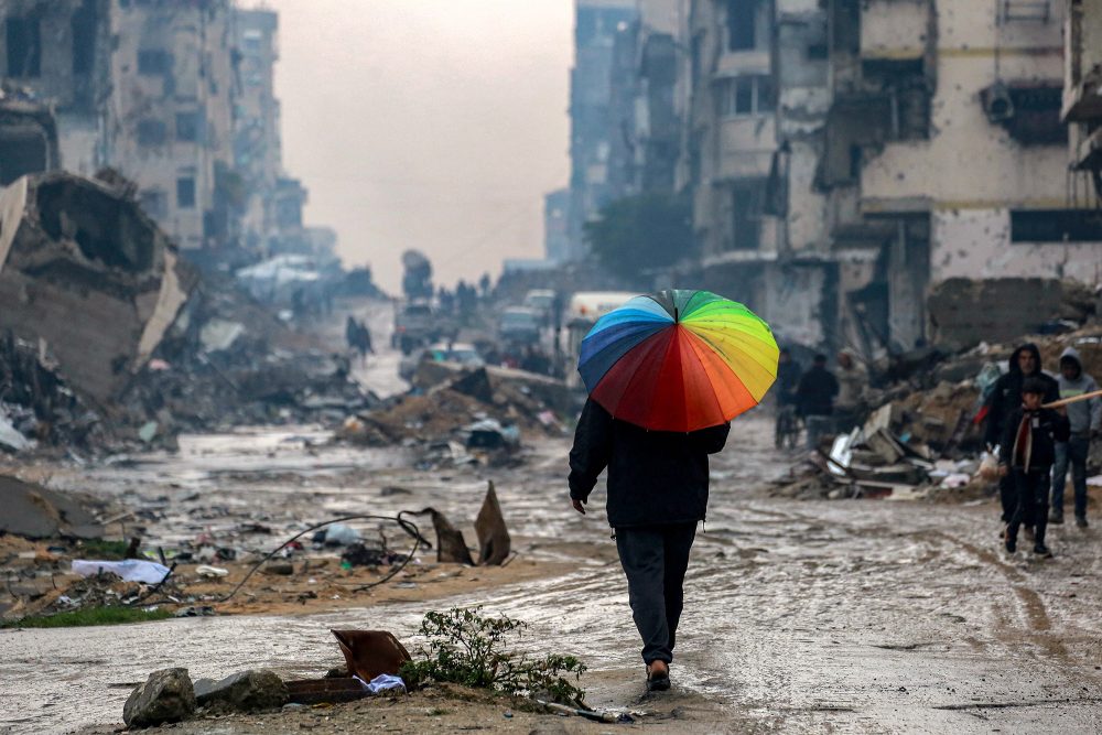 Mann mit Regenschirm in den Farben des Regenbogens inmitten zerstörter Häuser in Gaza-Stadt