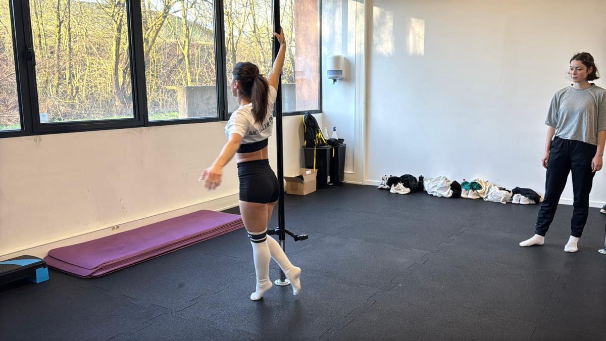 Eine Trainerin führt die Bewegung an der Poledance-Stange vor