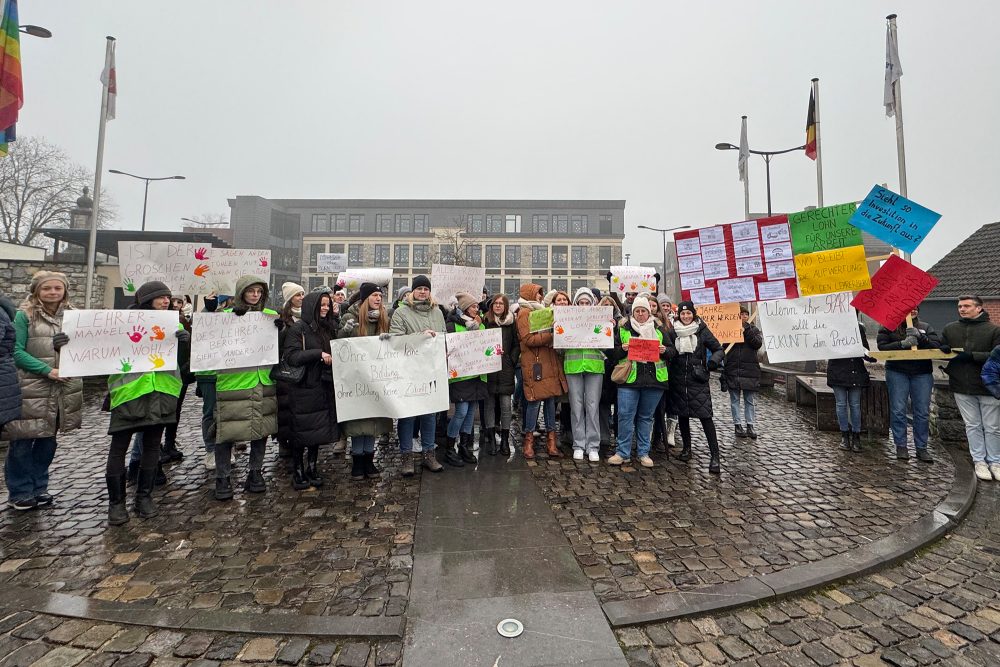 Demonstranten stehen auf dem Dorfplatz in Raeren und halten Poster und Schilder in die Höhe