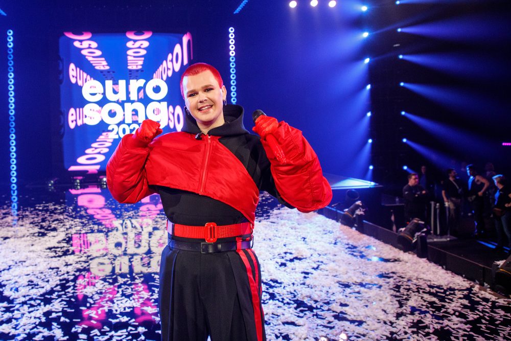 Red Sebastian steht nach dem Gewinn des "Eurosong 2025"-Finales auf der Bühne und reckt die Arme in die Höhe, er trägt einen schwarz-roten Dress und hat sehr kurze knallrot gefärbte Haare