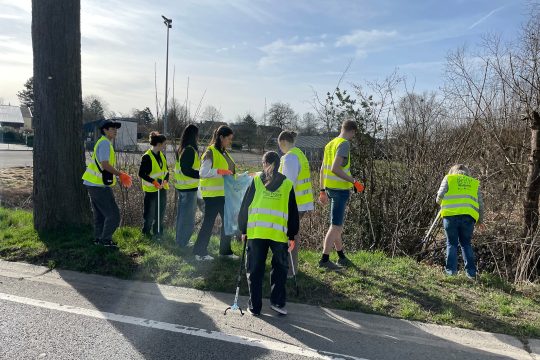 Schüler mit leuchtend-gelben Warnwesten sammeln mit Mülltüten und Müllgreifern ausgestattet Müll auf